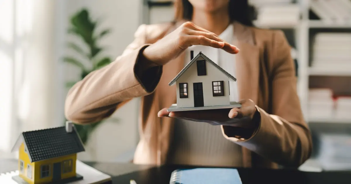 Hands holding model house for home insurance concept